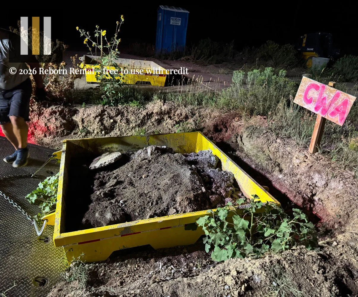 Truck winching a full yellow concrete washout pan onto a flatbed at night