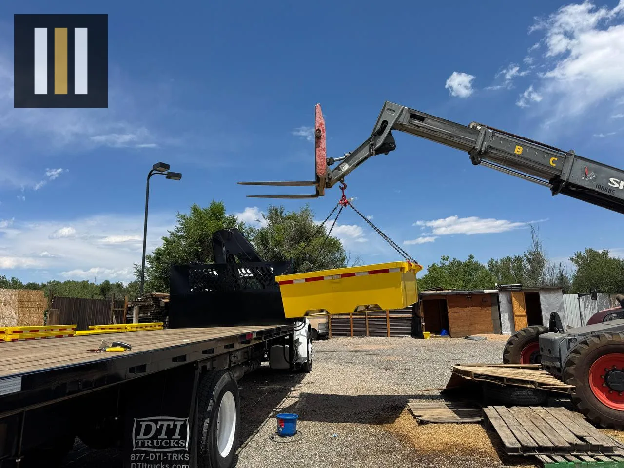 Telehandler using heavy lifting chains to position a yellow steel washout pan on a flatbed delivery truck.