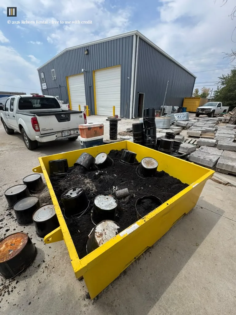 A yellow washout dumpster holding concrete residue positioned on a gravel lot near a commercial delivery vehicle.