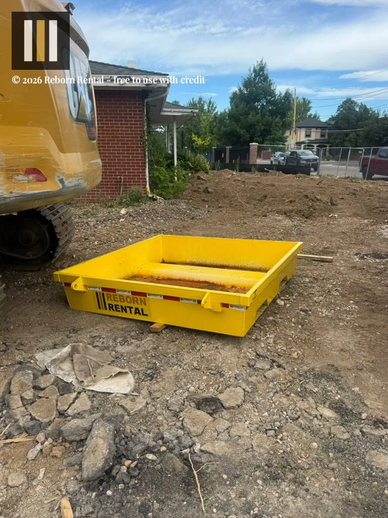 Watertight yellow steel washout pan stationed on a dirt jobsite beside heavy machinery