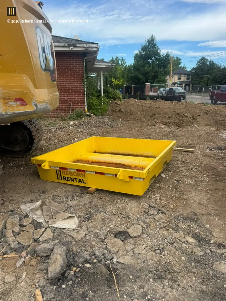 Yellow Reborn Rental concrete washout pan sitting on a dirt civil construction site next to an excavator.